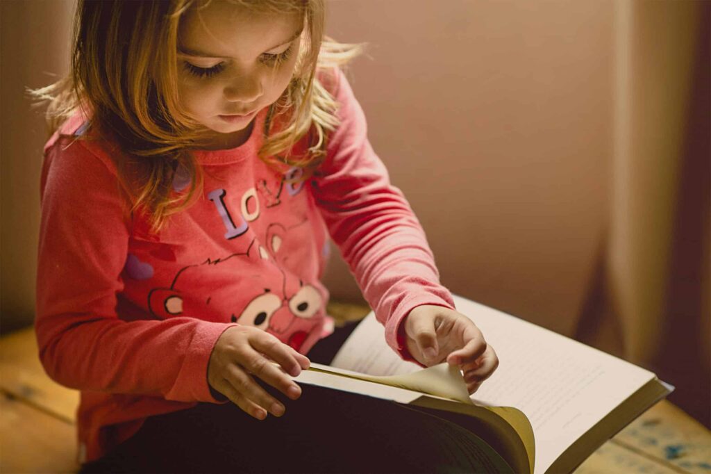 Girl in pink shirt turning pages reading a book
